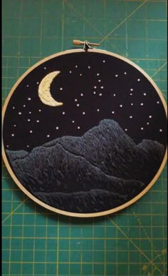 an embroidery project with mountains, stars and the moon in the sky on a cutting board