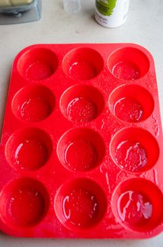 a red muffin tray sitting on top of a counter next to an empty cupcake pan