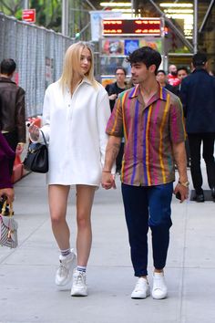 a man and woman walking down the street holding hands while wearing white shoes with colorful stripes