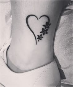 a black and white photo of a heart with flowers on the side of her ankle