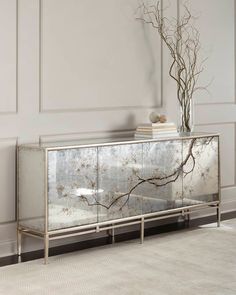 a mirrored cabinet with branches on it and a vase in the corner next to it