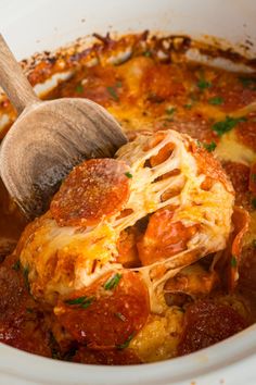 a wooden spoon in a white crock pot filled with lasagna sauce and cheese