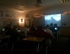 students are sitting at their desks in front of a projector screen with a mountain scene on it