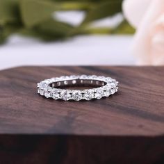 a close up of a wedding ring on a wooden surface with flowers in the background