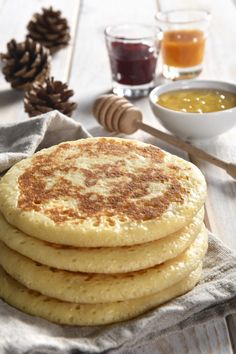 there is a stack of pancakes on the table next to some honey and syrups