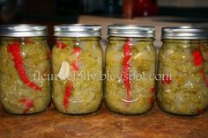 four jars filled with pickles sitting on top of a table