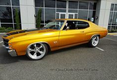 an orange muscle car parked in front of a building with large windows and chrome rims