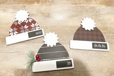 three hats with name tags on them sitting on a wooden table next to a christmas tree