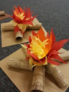 some paper flowers are sitting on top of brown envelopes with red and yellow leaves