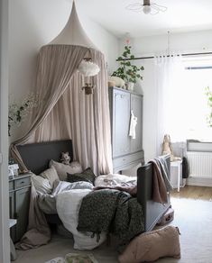 an unmade bed sitting in a bedroom next to a window with curtains on it