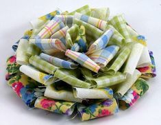 a bunch of fabric flowers sitting on top of a white tablecloth covered surface with multicolored stripes and floral designs