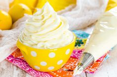 a yellow bowl filled with whipped cream on top of a colorful cloth next to lemons