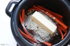 carrots and other vegetables in a slow cooker with a block of butter on top