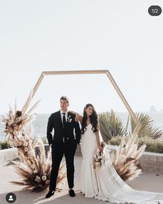 a man and woman standing next to each other in front of an arch with flowers