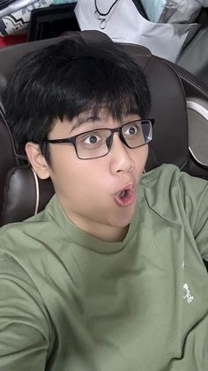 a young man wearing glasses making a funny face while sitting in a chair with his tongue out