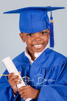 a young boy wearing a blue graduation gown and holding a white piece of paper in his hand