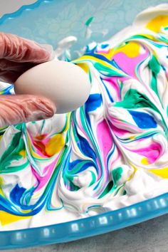 a person is spreading icing on a cake with an egg in the middle and colorful swirls