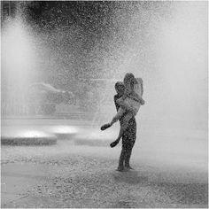 two people are playing in the water with their arms around each other and one person is holding an umbrella