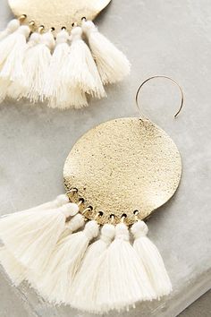 two pairs of earrings with tassels on top of each other, one in gold and the other in white