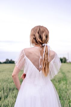 a woman in a white dress is standing in a field with her back to the camera