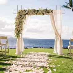 an outdoor ceremony setup with white flowers and drapes on the grass by the ocean