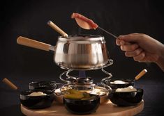 a person holding a spoon in front of a pot filled with food on top of a table