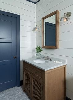 a bathroom with two sinks and a blue door in the back ground, next to a white wall