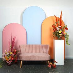 a pink couch sitting in front of a colorful wall with flowers and vases next to it