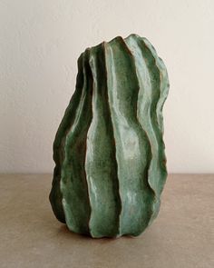 a green vase sitting on top of a table next to a white wall and floor