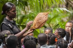 a woman holding up a piece of bread in front of a group of children who are all looking at it