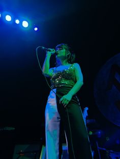 a woman standing on stage holding a microphone in her hand and singing into the microphone