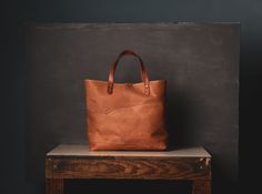 Our next installment of over-the-top tote. Subtle and sumptuous, made from top-grain Horween leather. Perfectly proportioned: 14 inch long, 12 tall and 6 inches wide. It will easily carry a day's supplies without breaking a sweat and it will look even better in ten years. Veg-tan leather, brass hardware, unlined, inside-loop. As tough as it looks and we back it with life-time warranty in case it needs repairs. Made at our shop, entirely by hand. Unrefined, one-and-only. Not returnable. Medium Leather Satchel With Handles, Medium Leather Bag With Leather Handles, Medium Leather Shoulder Bag For Errands, Vegetable Tanned Leather Tote Bag With Leather Backing, Everyday Tote Briefcase With Leather Backing, Large Leather Satchel With Top Carry Handle, Tooled Leather Bag, We Back, Horween Leather