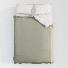 an unmade bed with two pillows and a blanket on top of it, in front of a white wall