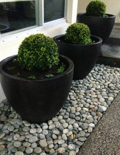 three large black planters sitting next to each other in front of a house with rocks on the ground