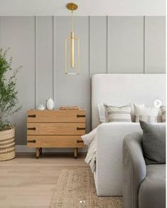 a white couch sitting next to a wooden dresser in a living room under a golden light fixture