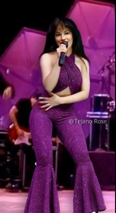 an image of a woman in purple outfit singing into a microphone at a concert or show