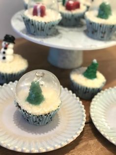 cupcakes decorated with frosting and christmas trees on white plates, sitting on a table