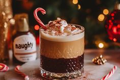 a hot chocolate drink with whipped cream and candy cane on the rim in front of a christmas tree