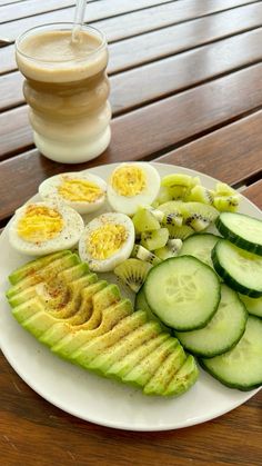 sliced cucumbers and hard boiled eggs on a white plate next to a drink