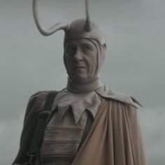 a man dressed in costume and holding a large metal object on his head, standing outside