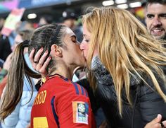 two women kissing each other in front of a group of people at a soccer game