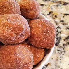 a bowl filled with sugar covered donuts on top of a marble countertop next to a granite counter