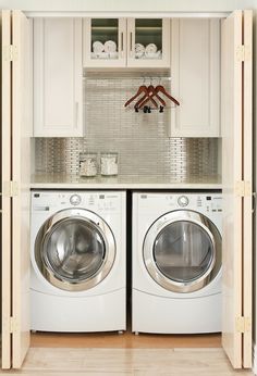 a washer and dryer in a small room with white cupboards on the wall