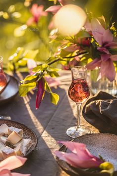 a table topped with plates and glasses filled with wine next to flowers in vases