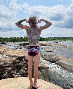 a woman standing on top of a rock next to a body of water with her hands behind her head