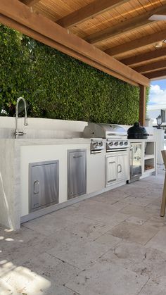 an outdoor kitchen with stainless steel appliances under a pergolated roof