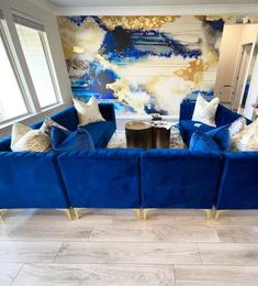 a living room filled with blue couches next to a wall covered in art work