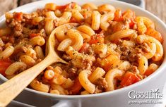 a white bowl filled with pasta and meat on top of a wooden table next to a spoon