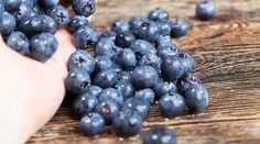 blueberries are being picked from the ground by someone's hand on a wooden table