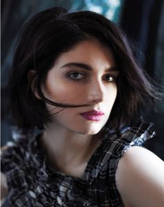 a woman with black hair and pink lipstick looks into the distance while posing for a photo